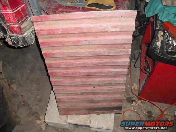 Red corrugated metal panel leaning against concrete blocks, with a red vehicle tail light visible to the left