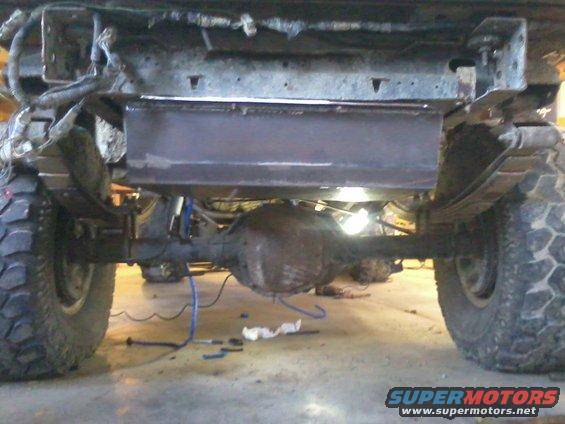Underside view of a vehicle's rear axle and leaf springs, with a newly welded metal skid plate installed