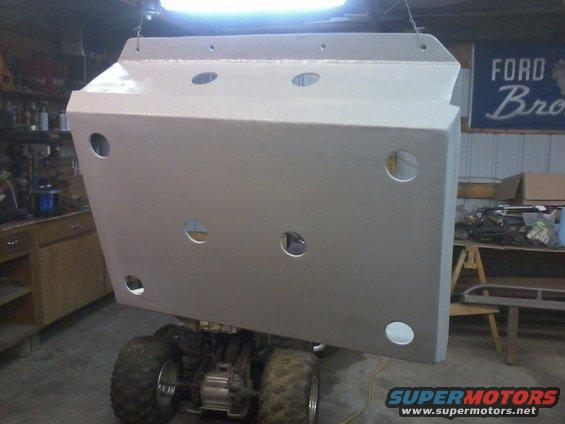 Large metal skid plate hanging above an ATV in a garage. A 'Ford Bronco' banner is visible on the wall