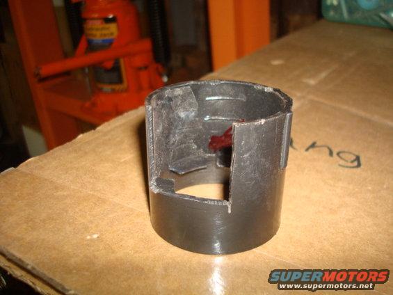 black plastic part with red stuff inside, sitting on cardboard. Orange hydraulic jack in background