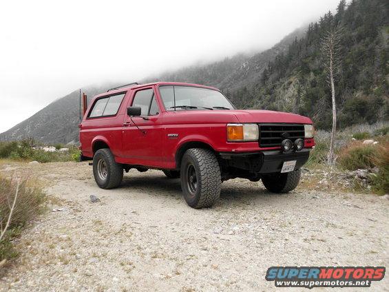 Red Ford Bronco with aftermarket bumper and off-road tires parked on a dirt road