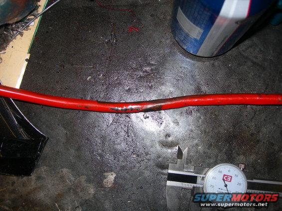 Damaged red cable measured with a caliper and dial indicator on a workbench