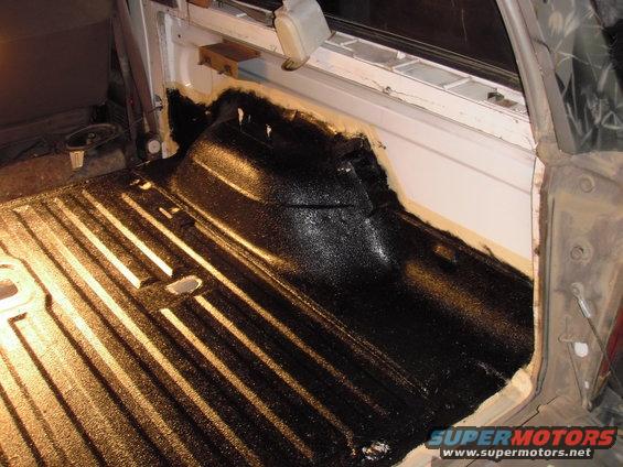 Truck bed with black liner being applied, showing ribbed floor and wheel well area