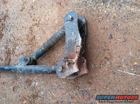 Damaged metal suspension component with a broken bracket, lying on the ground