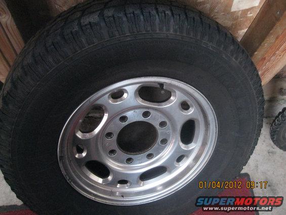 Tire on a silver alloy wheel with eight large oval cutouts and ten smaller bolt holes