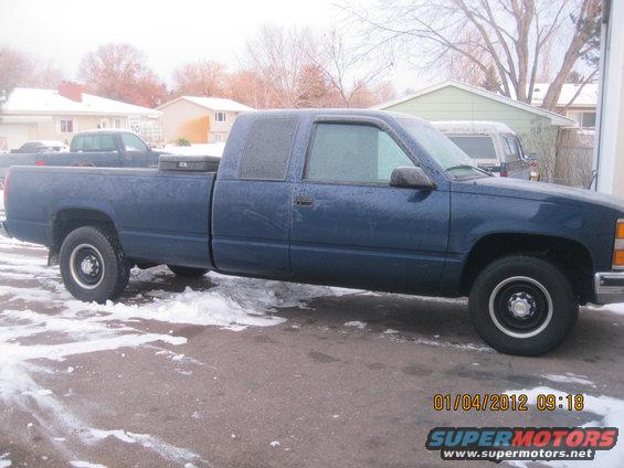 Blue pickup truck, side view. Another truck is visible behind it