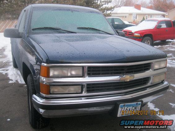 Dark blue pickup truck with a chrome grille and bumper. Red pickup truck in background. License plate reads 716 GMU