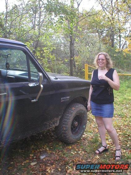 Woman standing next to a black 1989 Ford Bronco in a wooded area