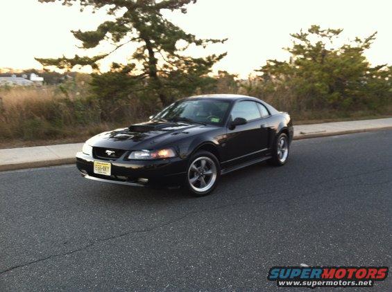 Black 2002 Ford Mustang coupe parked on asphalt road with trees and sky in background