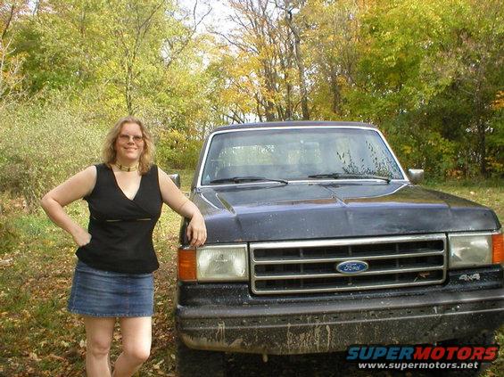 Dark SUV with a chrome grille and Ford emblem, 4x4 badge on fender. Woman in black top and denim skirt leans on it