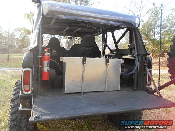 Black off-road vehicle's open tailgate reveals a large metal fuel tank and a red fire extinguisher mounted on the side