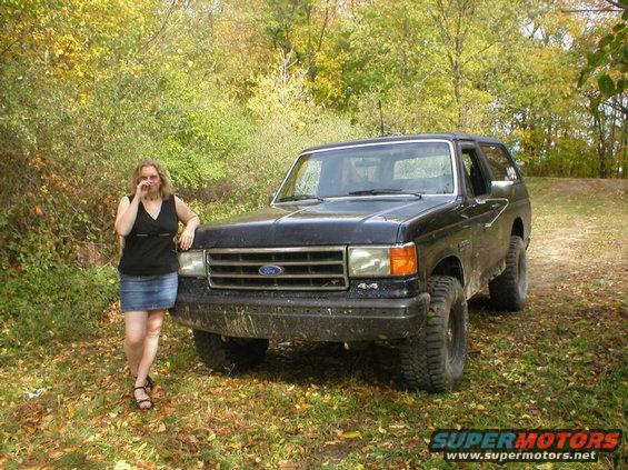Black Ford Bronco parked on a dirt path with a woman standing next to it