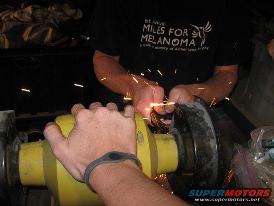 Person grinding metal with sparks flying, another person's hand visible