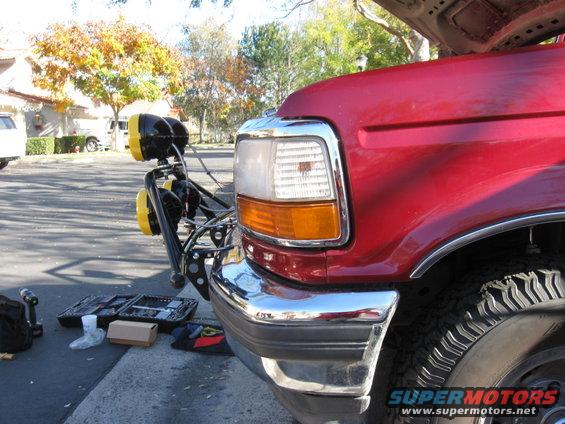 Red Ford truck front fender and bumper with chrome accents and a light bar. Tools are on the ground