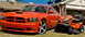 2009 Dodge Charger - A bright orange Dodge Charger SRT8 is parked on the lawn next to a riding mower in front of a suburban home.