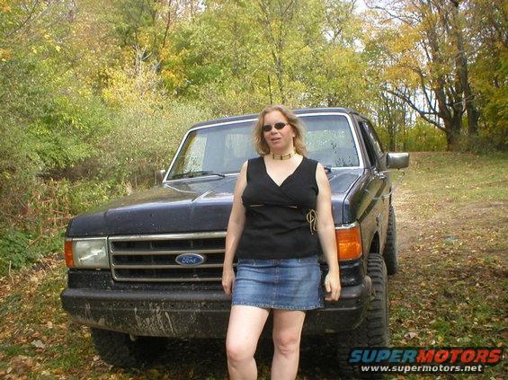 Woman in black top and denim skirt in front of a black 1987 Ford Bronco