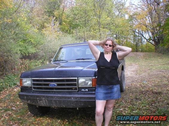 Woman posing in front of a dark blue Ford Bronco. The Bronco has a "4x4" badge on the fender