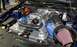 2012 Ford Mustang - The engine bay of a dark blue Ford Mustang shows a prominent supercharger and custom intake system.