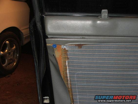 Car door panel with torn fabric and visible rust, next to a white car's wheel