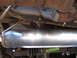 1996 Ford Bronco - Undercarriage view of a vehicle's exhaust system, showing a shiny muffler and rusty frame components.