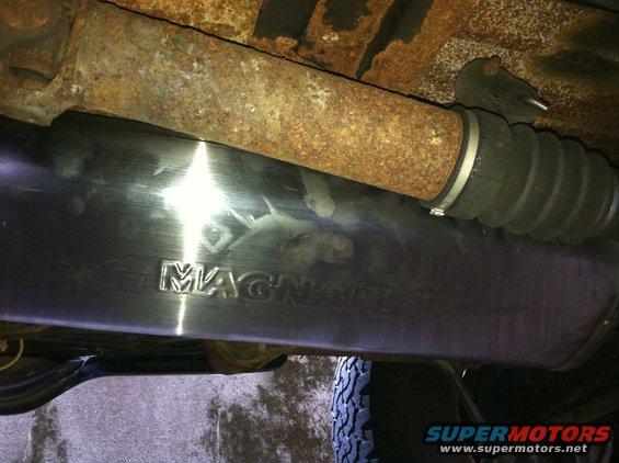Exhaust pipe with "MAGNAFLOW" logo, rusty driveshaft, and rubber boot