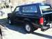 1996 Ford Bronco - A black Ford Bronco is seen from the side, parked in a lot with trees and a fence in the background.