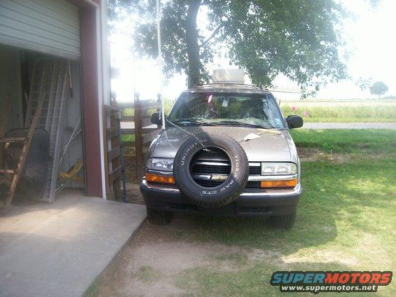 Silver SUV with spare tire mounted on front, parked next to garage