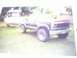 1993 Ford Bronco - A dark blue Ford Bronco is parked on a grassy area, with a boat on a trailer visible behind it.