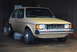 1983 Volkswagen Rabbit - A tan 1983 Volkswagen Rabbit with a yellow hood is parked indoors, showing its front end with a missing grille.