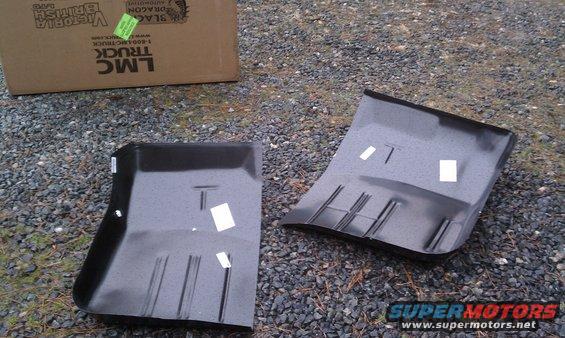 Two black car floor pans on gravel, one with a box labeled "LMC TRUCK" behind it