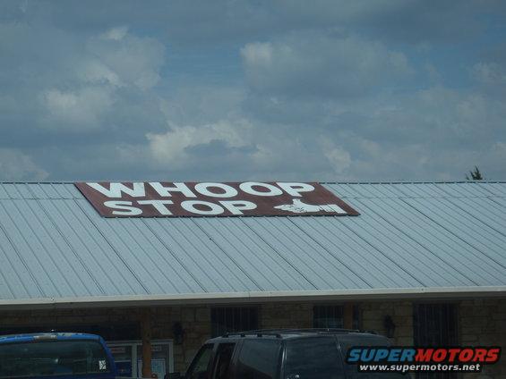 Building with "WHOOP STOP" sign and a blue truck and black SUV