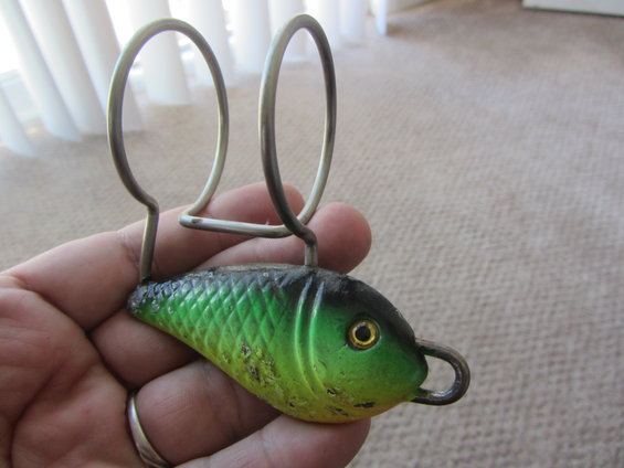 Hand holding green and black fish-shaped fishing lure with metal loops