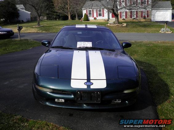 Dark green Ford Probe with white racing stripes parked in a driveway. A sign is on the windshield