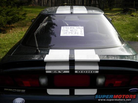 Rear view of a black 1997 Ford Probe with white racing stripes and a note on the back window