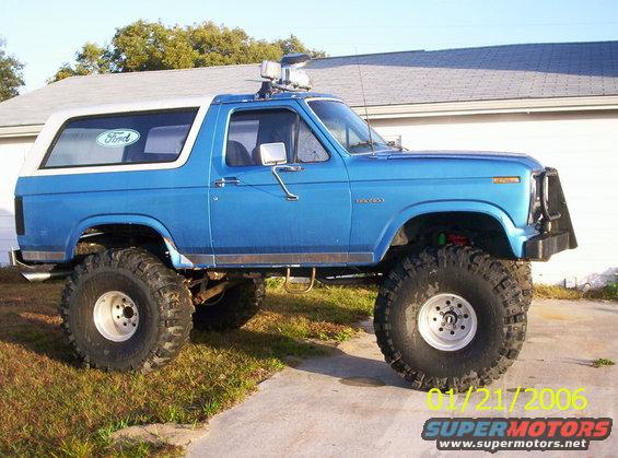 Blue Ford Bronco with white roof, lifted suspension, and large off-road tires, seen from the side