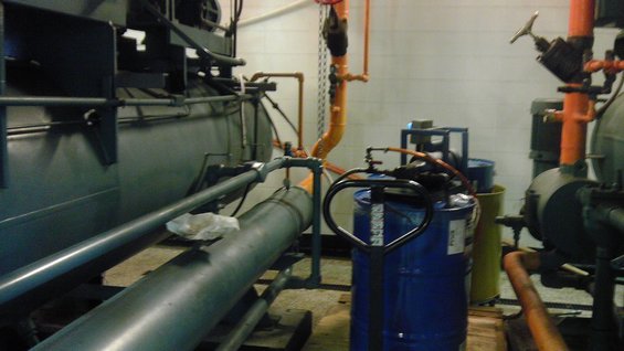 Industrial pipes and machinery in a room with blue barrels and a pallet jack
