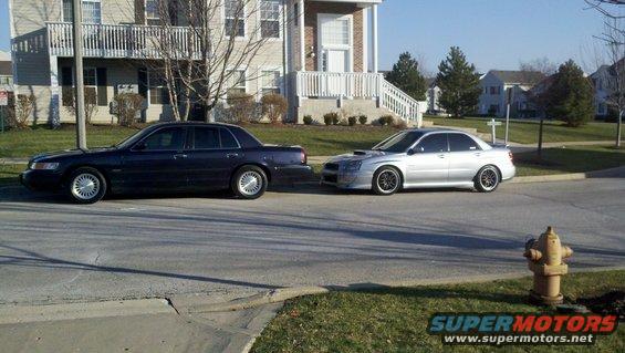 Dark sedan and silver Subaru WRX parked on street in front of apartment buildings