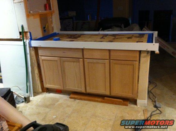Kitchen island with light wood cabinets and plywood countertop covered in blue tape