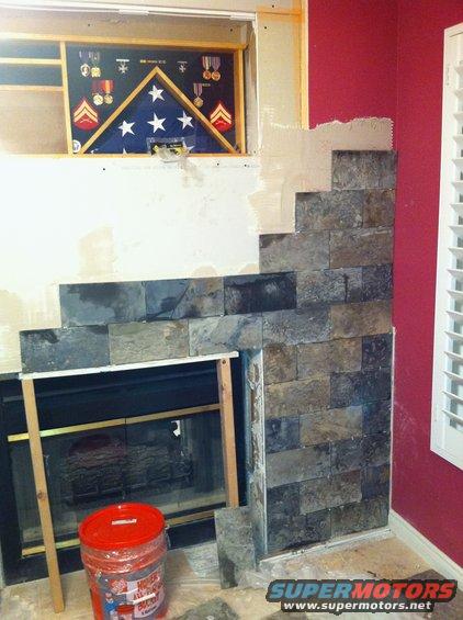 Fireplace renovation in progress, showing stone tile installation and a shadow box with a folded American flag and military medals