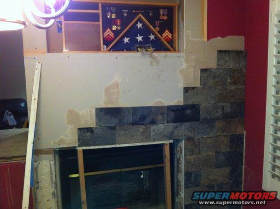 fireplace under construction with stone tile and a framed flag with medals above