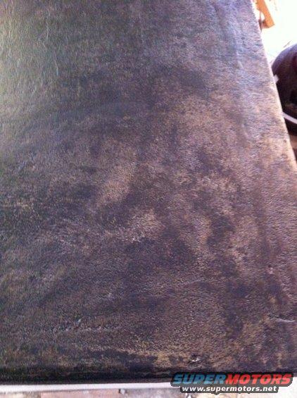 close-up of dark, textured material, possibly car seat or floor mat, showing wear and discoloration