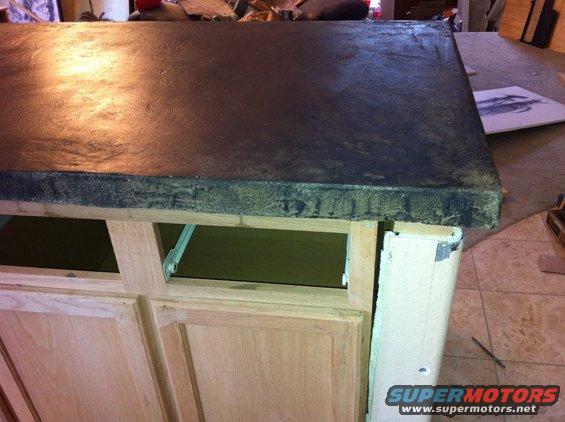 Dark countertop on unfinished wooden cabinets, with visible construction materials