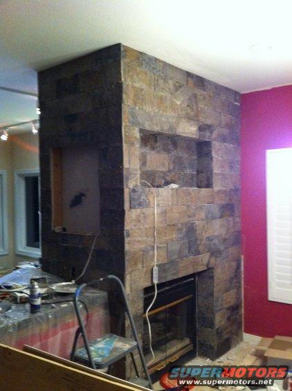 Stone fireplace with a gas insert is under construction, with tools and materials nearby