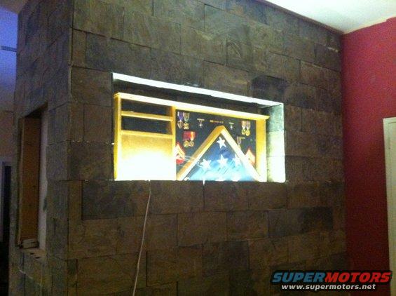 Display case with folded American flag and military medals mounted in a stone wall