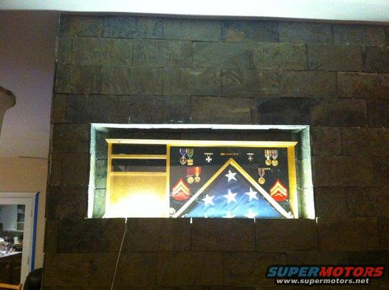 Display case with folded flag and military medals mounted on a stone wall