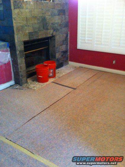 Fireplace with stone facade and two red buckets on floor, next to unfinished cork flooring