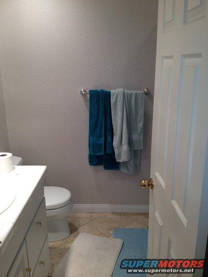 Bathroom with toilet, vanity, and towels on a rack. A door is ajar