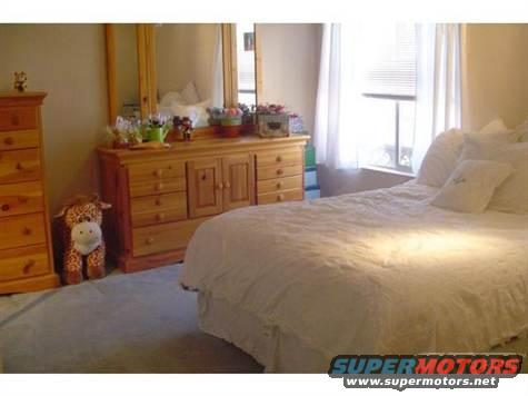 Bedroom interior with a wooden dresser, a stuffed giraffe toy, and a made bed with white linens