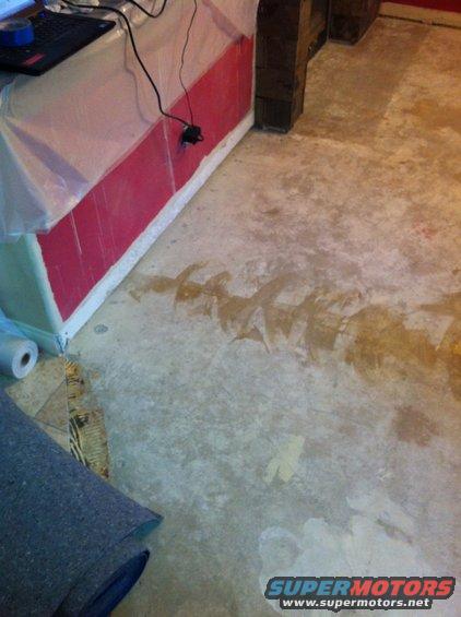 Unfinished basement floor with water stains and a roll of carpet