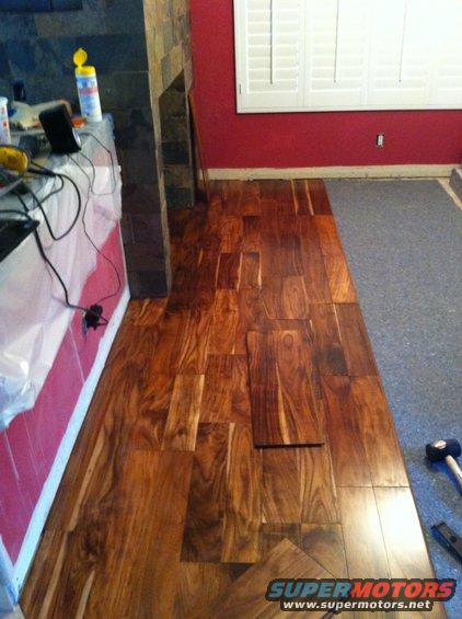 hardwood flooring being installed next to a carpeted area, with a fireplace and red wall in the background